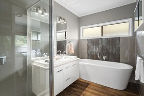 A modern bathroom with a glass shower enclosure, a freestanding bathtub, and a vanity with a mirror.