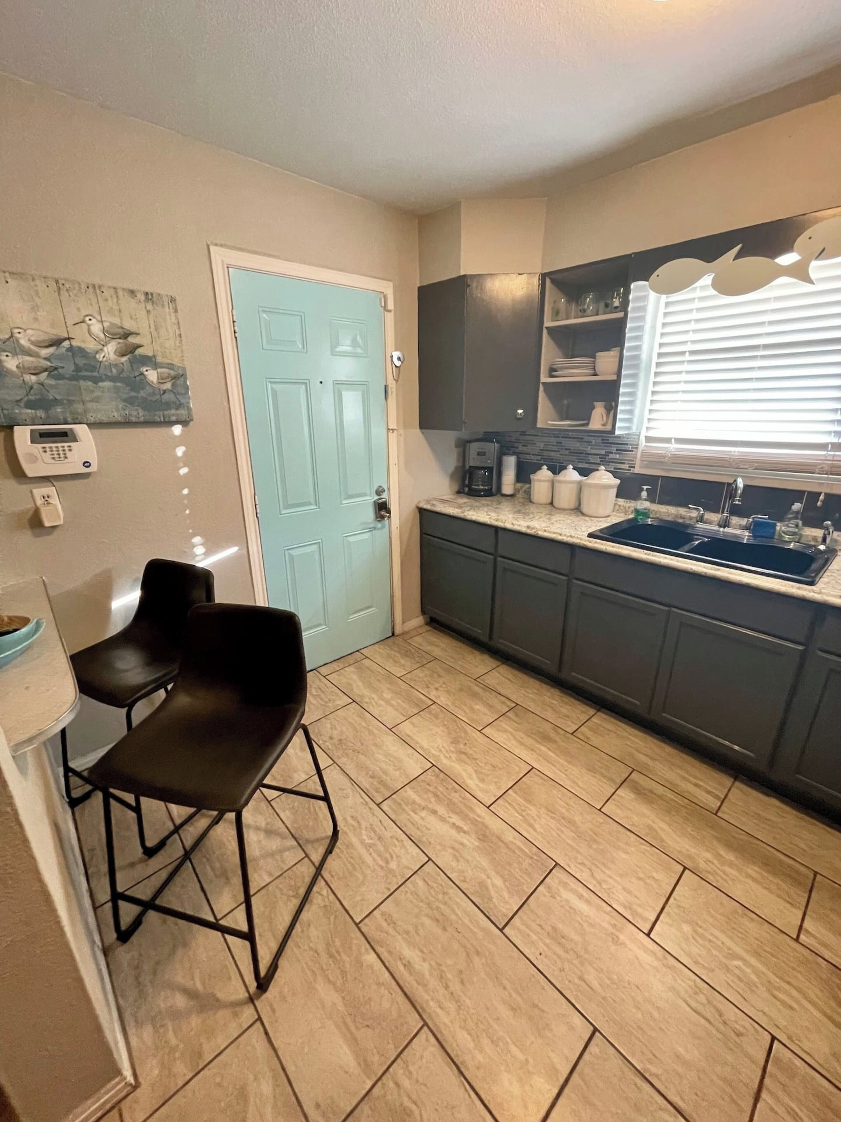 A compact kitchen with a blue door, a coffee maker, and a window with blinds.