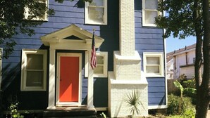Une maison à deux étages avec une porte rouge, des boiseries blanches et un petit porche à l’avant.