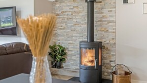 A modern living room with a stone wall, a black wood-burning stove, a sofa, a coffee table, and a vase with dried plants. - "Alvira" - 30km from the sea by Interhome (Toftlund)