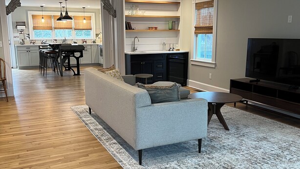 A modern living room with a grey sofa, a TV, and a kitchen in the background.