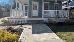 A two-story house with a porch, a front door, and a small front yard with a stone pathway.