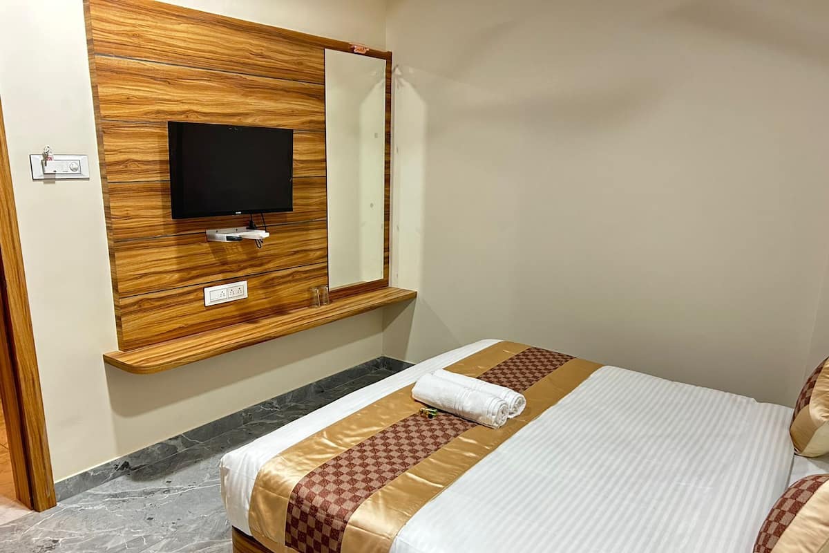 A hotel room with a wooden wall panel, a flat-screen TV, a bed with a patterned bedspread, and a marble floor.
