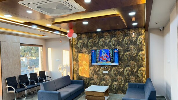 A modern waiting area with blue sofas, a TV on the wall, and a patterned wallpaper. - HOTEL SHREE HARI (Dwarka)