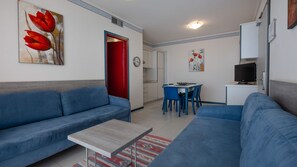 Un salon avec un canapé bleu, une petite table et un coin repas avec des chaises bleues.