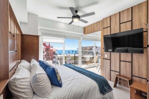 A bedroom with a bed, a ceiling fan, a TV, and a balcony with a view.