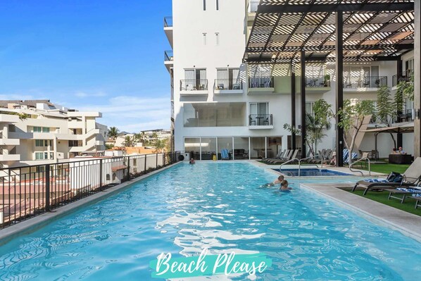 A swimming pool with a sunshade structure, surrounded by a multi-story building with balconies and a view of neighboring buildings.