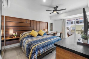 A modern hotel room with a large bed, a desk, a ceiling fan, and a view of the city.