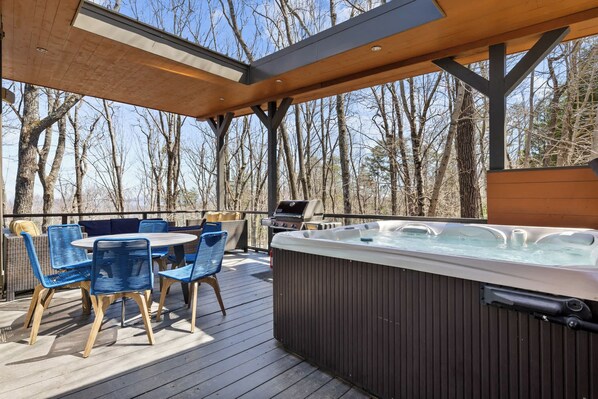 Une terrasse en bois avec un jacuzzi, des chaises bleues et un barbecue.