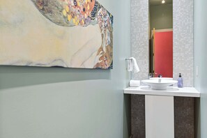 Une salle de bain avec un grand tableau abstrait, un lavabo blanc, un miroir et une porte rouge.