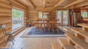 Ein Holzblockhaus-Interieur mit Essbereich, Holzbänken, einer Küche und großen Fenstern.
