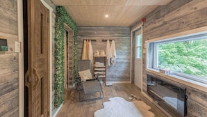 Ein rustikales Blockhaus-Interieur mit Holzwänden, einem großen Fenster, einem Kamin, einem Fellteppich und einer Bank.