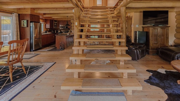 Ein rustikales Blockhaus-Interieur mit einer zentralen Treppe, Holzdielen, einer Küchenzeile und einem Wohnzimmer mit einer Ledersofa.
