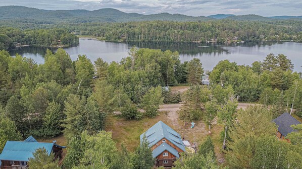A cabin surrounded by dense forest, a lake, and distant mountains.