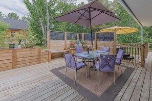 A wooden deck with a table and chairs, surrounded by a wooden fence and trees.