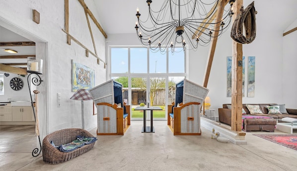 A spacious room with a large window, wicker furniture, a chandelier, and a rustic wooden beam.
