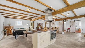 Una habitación amplia con mesa de billar, vigas de madera, una isla grande con estufa y un área de comedor.