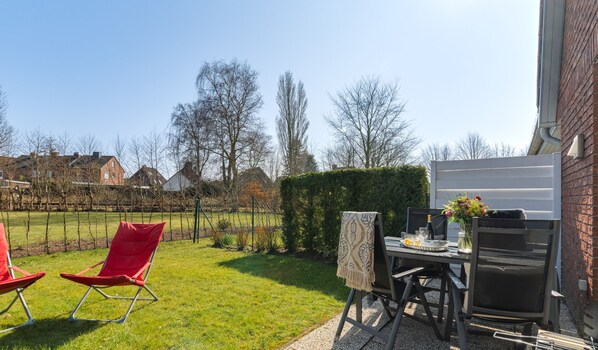 A patio with a table set for two, a red chair, and a grill.