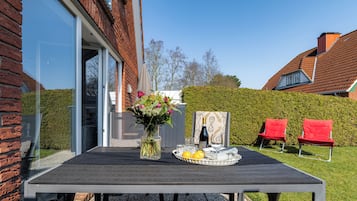 Eine Terrasse im Freien mit Esstisch, Blumen in einer Vase und zwei roten Stühlen.