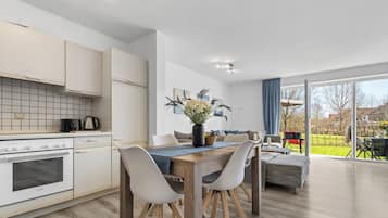 Eine moderne Küche mit weißen Schränken, einem Holzespeisetisch und Blick ins Freie durch große Fenster.
