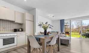 Una cocina moderna con armarios blancos, una mesa de comedor de madera y vistas al exterior a través de amplios ventanales.