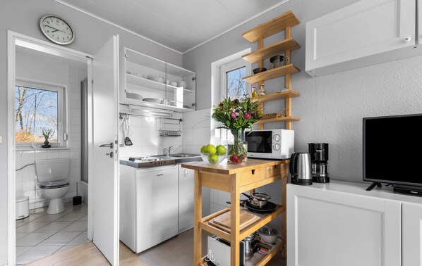 Une cuisine moderne avec des meubles blancs, une étagère en bois, un four à micro-ondes et une machine à café.