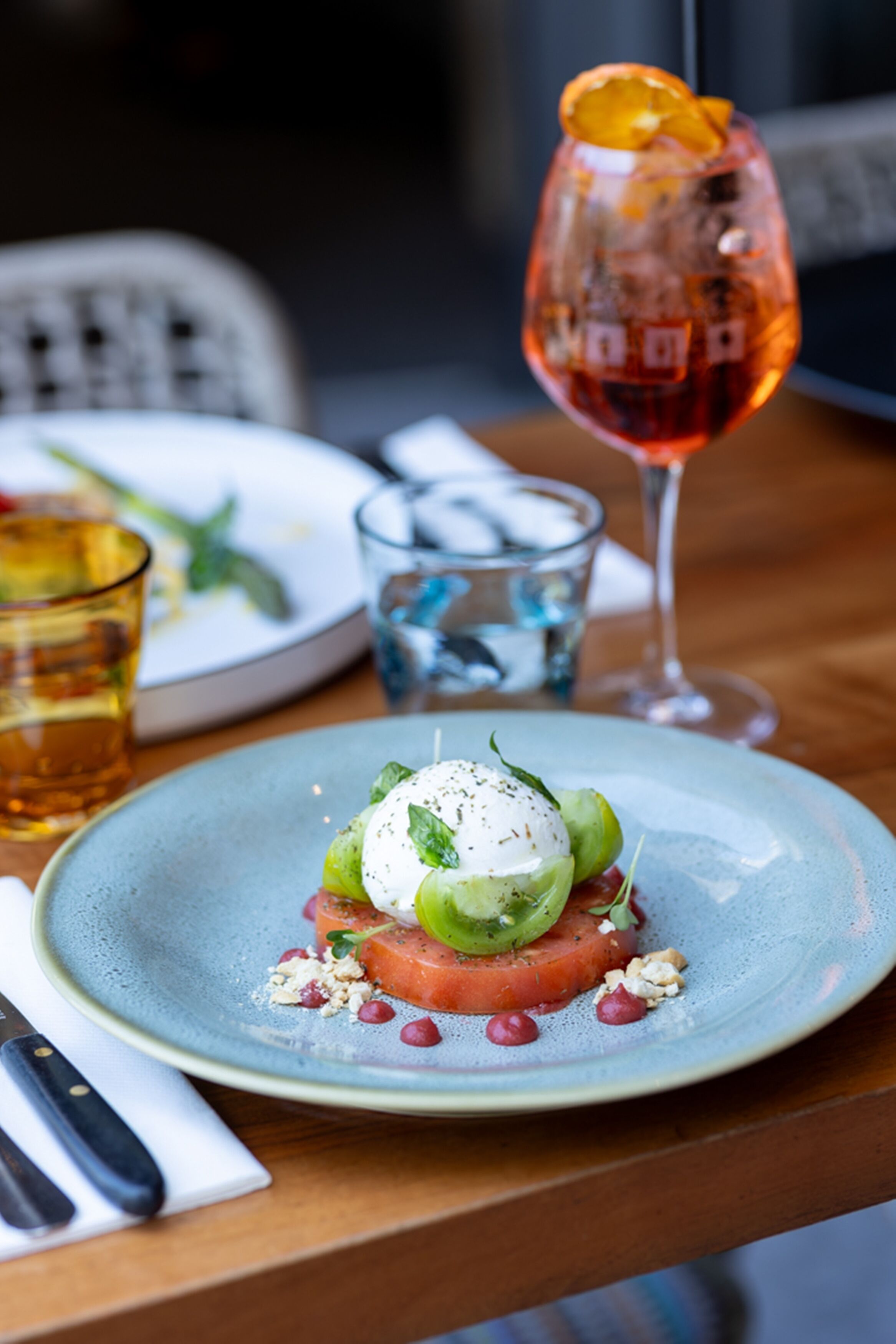 Ein Desserteller mit pochiertem Ei, Tomate und Grünzeug, dazu ein Glas Rotwein und ein Glas Wasser.