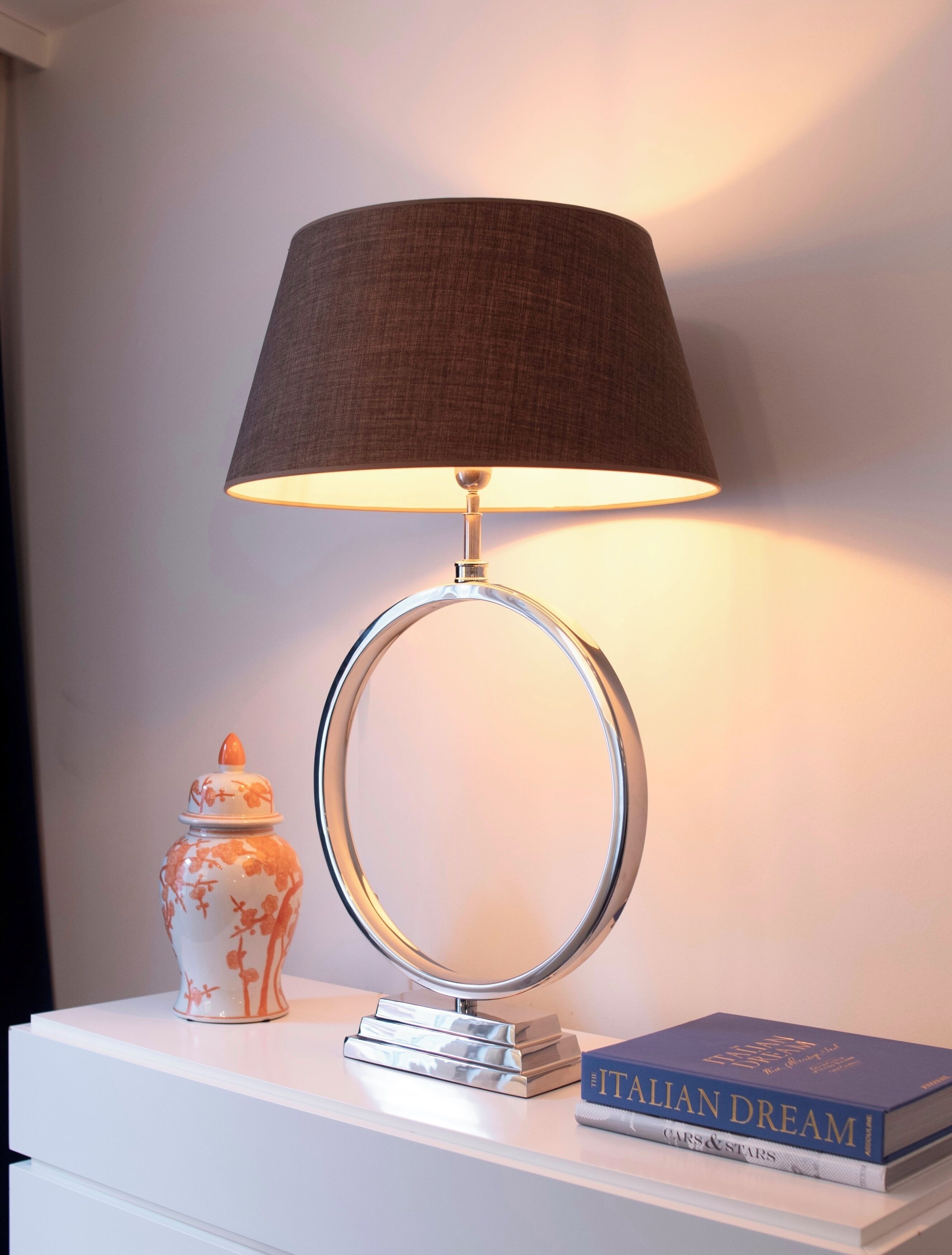A lamp with a circular base and a conical shade, a ceramic vase with floral patterns, and a book titled "ITALIAN DREAM" on a white surface.
