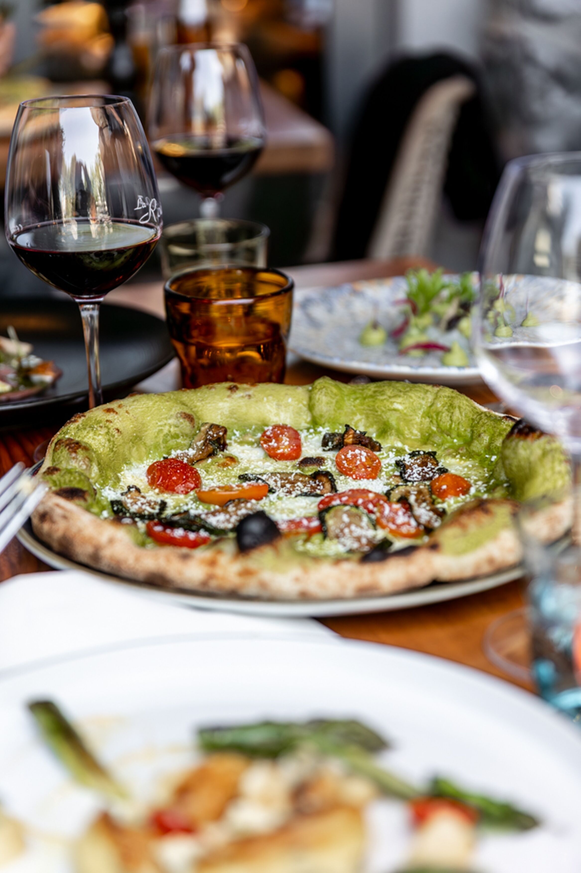 A dining table with a pizza, wine glasses, and a glass of beer.