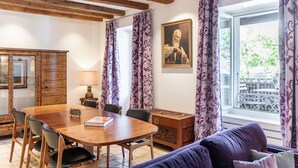 A dining area with a wooden table and chairs, a sofa, a cabinet, and a window with curtains. - Rouvenaz Appartements (Montreux)