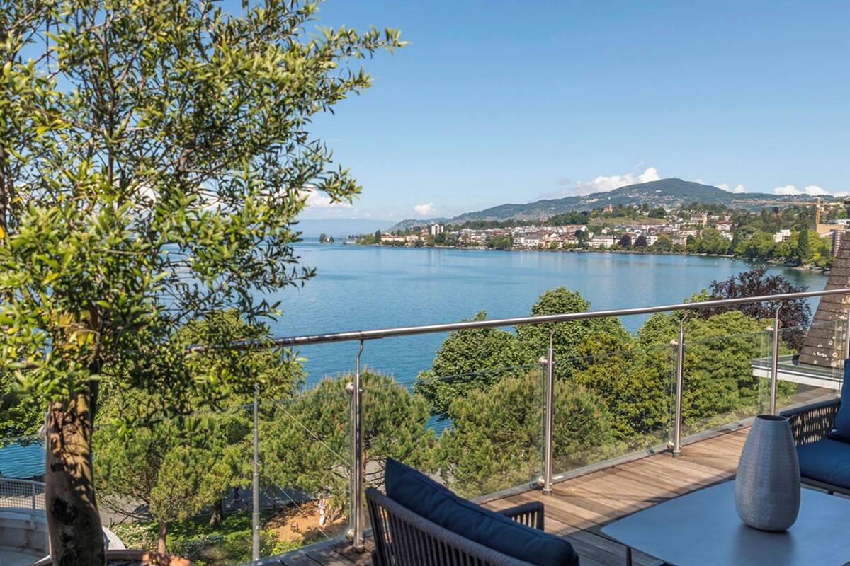 Una terraza con vistas a un lago, rodeada de árboles y un paisaje urbano distante.
