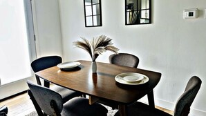 A dining area with a wooden table, four chairs, a vase with dried plants, and two wall-mounted mirrors.