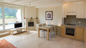 A modern kitchen with a dining area, a fireplace, and a large window overlooking a scenic landscape. - The Cristal apartment house is situated in a quiet, sunny and central location (Leukerbad)
