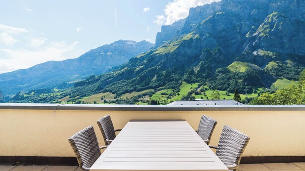A terrace with a table and chairs, overlooking a mountainous landscape. - The Cristal apartment house is situated in a quiet, sunny and central location (Leukerbad)