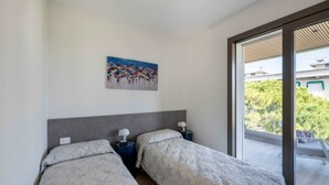 Un dormitorio con dos camas, un cuadro en la pared y vistas a través de un ventanal corredero.