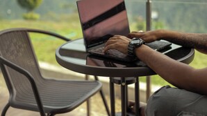 Une personne utilise un ordinateur portable sur un balcon d’où l’on peut admirer des montagnes.