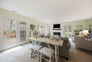 A spacious living area with a dining table, cushioned seating, and a television mounted on the wall.