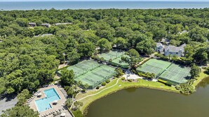 An aerial view of a property with tennis courts, a swimming pool, and a large body of water.