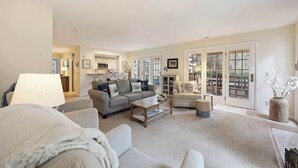 A spacious living room with a grey sofa, a coffee table, and a view through large glass doors to an outdoor patio.