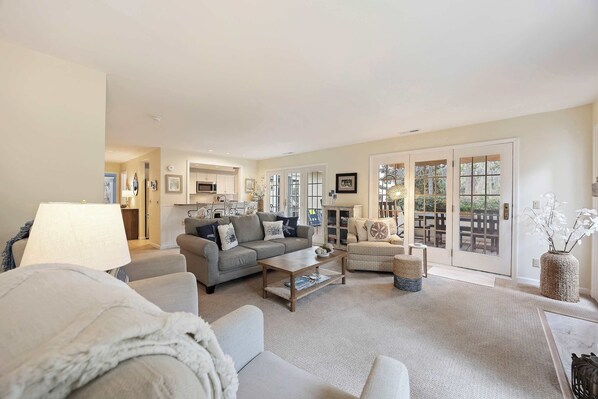 A spacious living room with a grey sofa, a coffee table, and a view through large glass doors to an outdoor patio. - Serene Golf & Lagoon Escape 235 Evian Villa in Shipyard (Hilton Head Island)