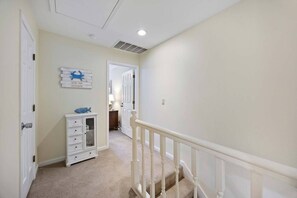 A hallway with a white door, a white dresser with drawers, a blue fish decoration, and a staircase with white balusters.