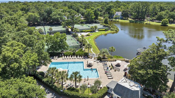 An aerial view of a resort with a swimming pool, tennis courts, and a lake.