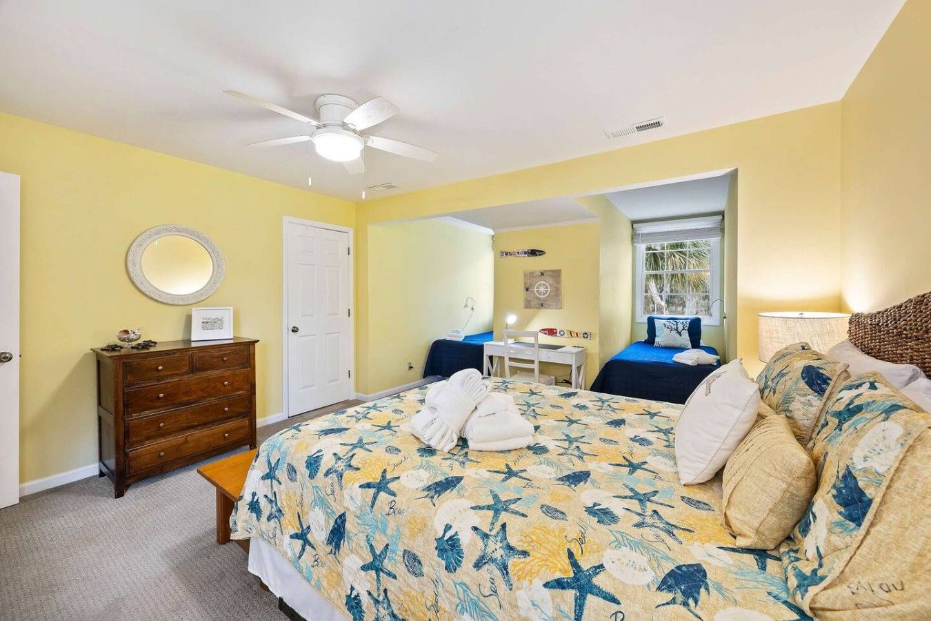 A bedroom with a bed, dresser, desk, chair, and a ceiling fan.
