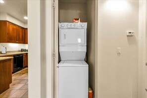 A compact laundry room with a stacked washer and dryer, wooden cabinets, and a tiled floor.