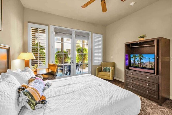 A hotel room with a large bed, a TV, a chair, and a balcony with a table and chairs.