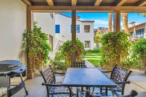 An outdoor patio with a table and chairs, surrounded by lush greenery and a view of neighboring buildings.