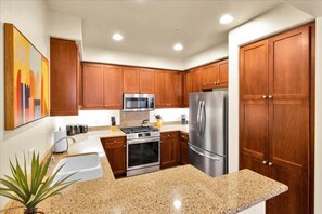 A modern kitchen with wooden cabinets, stainless steel appliances, granite countertops, and a potted plant.