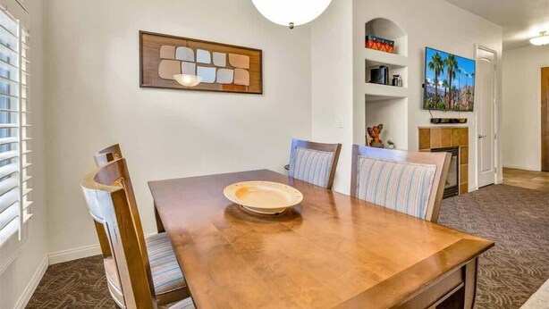 A dining area with a wooden table, striped chairs, and a decorative light fixture. - Desert Bloom A | 1BR Legacy Villa (La Quinta)