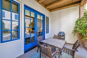 A patio with a table and chairs, a grill, and a blue door.