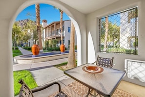 Uma área de pátio com mesa e cadeiras, vista para uma piscina e um edifício ao fundo.